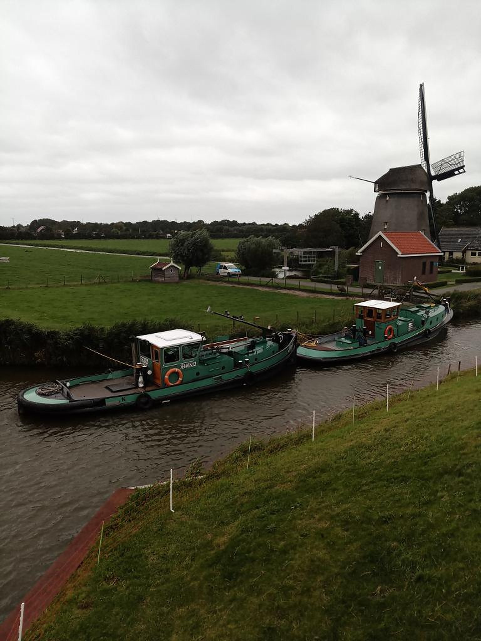 De duwsleepboten Trio en Nienke van Trionaut naast elkaar in een vaart bij een molen